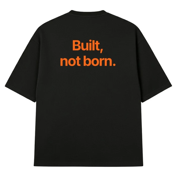 Crna oversize majica, na leđima narandžasta rečenica „Built, not born.“